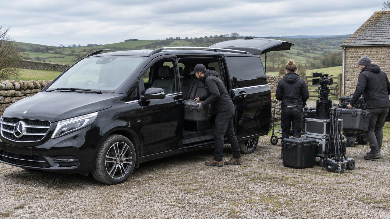 Film crew loading camera cases into a black Mercedes V-Class at a rural location shoot